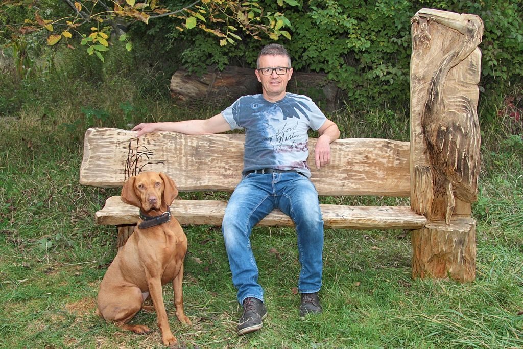 Bernd Messemer sitzt auf einer selbst gefertigten Holzbank aus massivem Eichenholz
